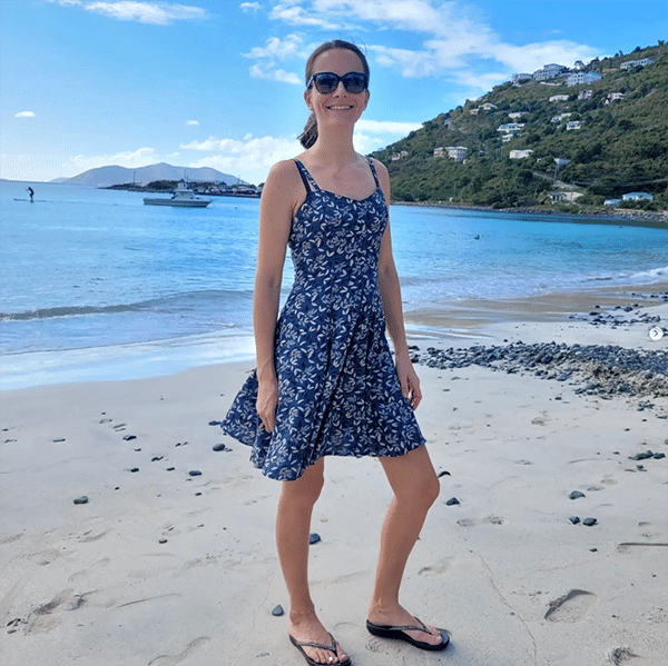 Sirius summer dress pattern in a blue viscose, modeled by a young woman with a ponytail on a beach