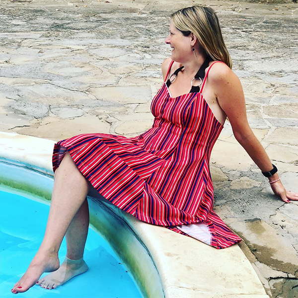 Sirius slip dress sewing pattern in a pink striped stretch fabric, modeled by a woman sitting with her feet in a pool.
